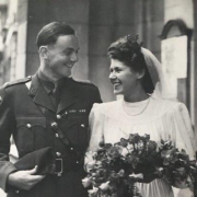 Black and white wedding picture of a man in military uniform and a bride in a white dress with an bunch of flower, they are both smiling.