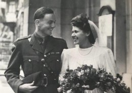 Black and white wedding picture of a man in military uniform and a bride in a white dress with an bunch of flower, they are both smiling.